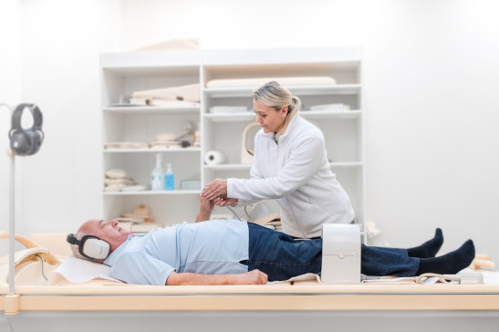 MFA kümmert sich um ältereren Patient mit Kopfhörern auf Liege