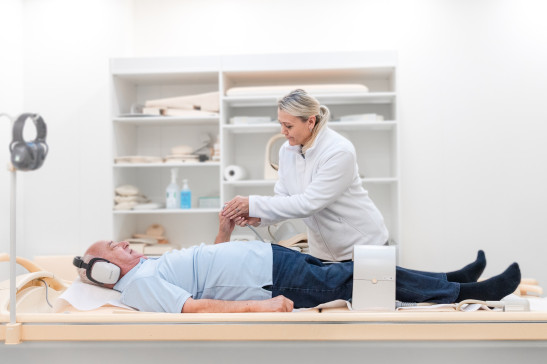 MFA kümmert sich um ältereren Patient mit Kopfhörern auf Liege